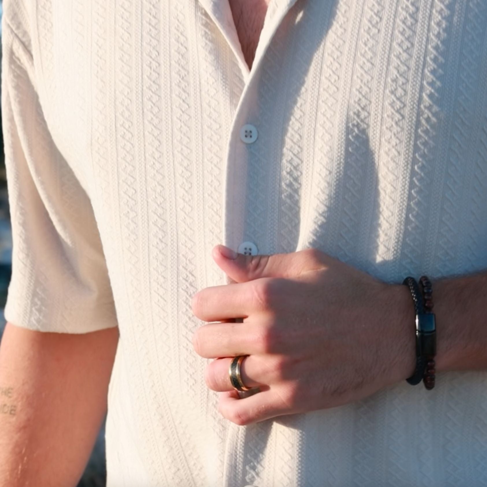 man wearing a textured white shirt with gold ring and leather bracelet that can be engraved