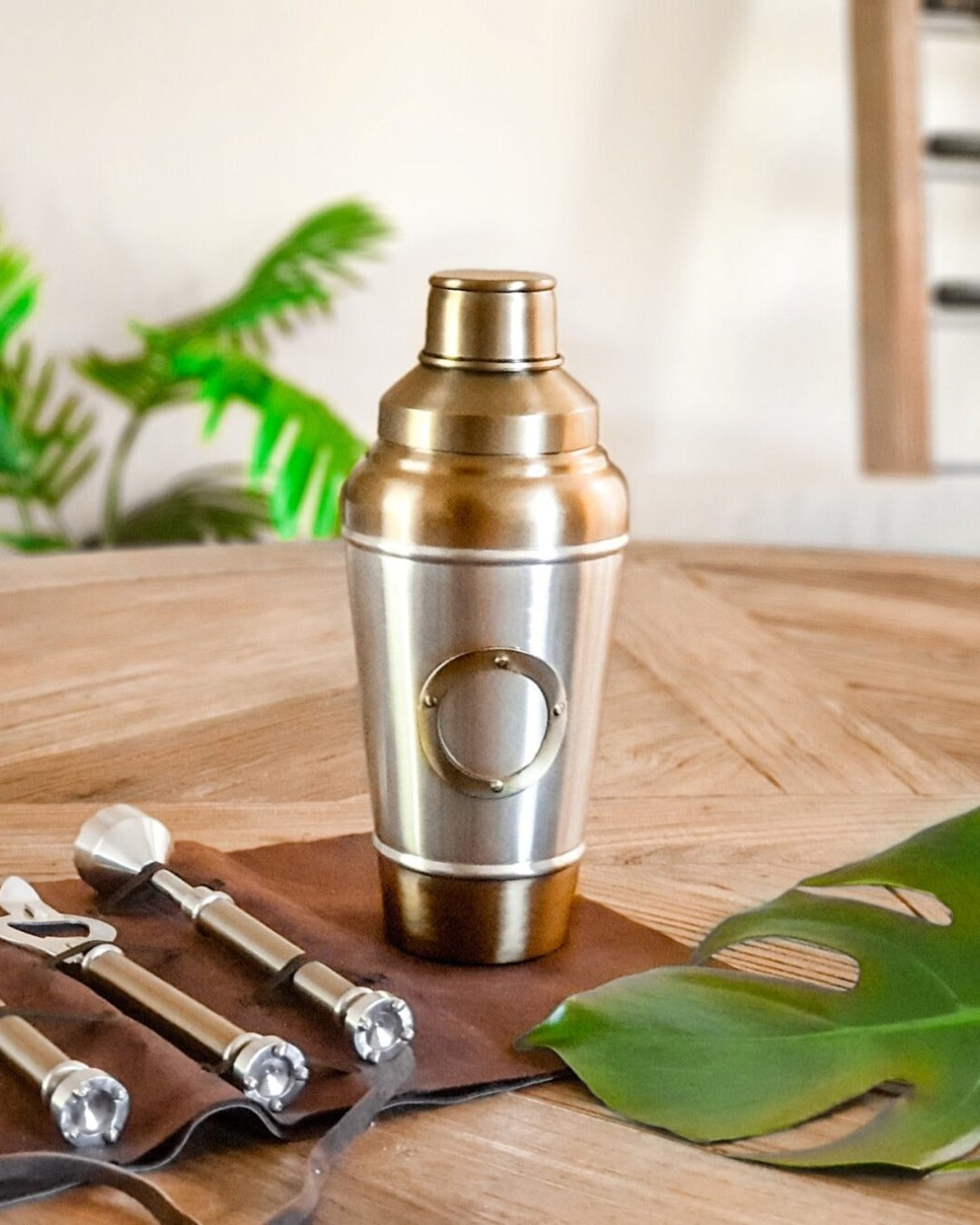 Personalised Brass cocktail shaker on a wooden surface with bar tools and leaves.