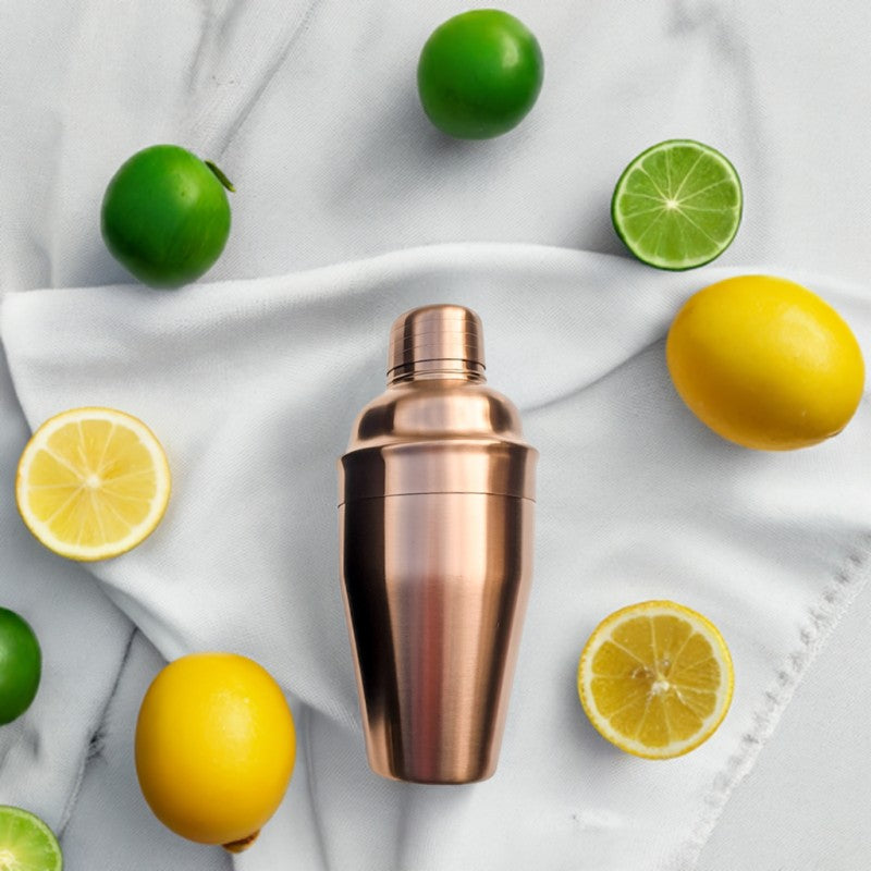 Copper cocktail shaker surrounded by lemons and limes on a white fabric background