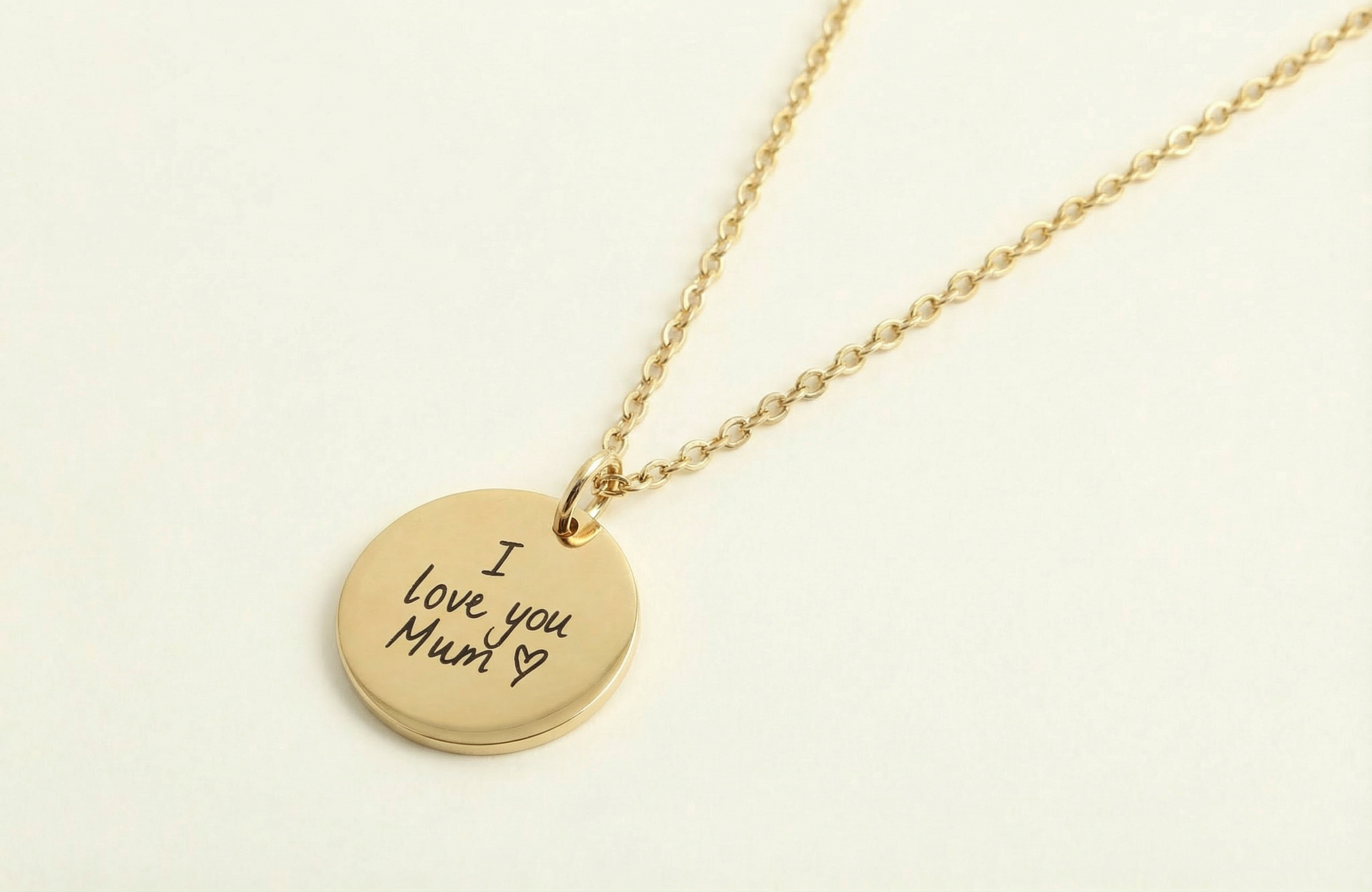 Gold necklace with a round pendant engraved with 'I love you Mum' on a light beige background