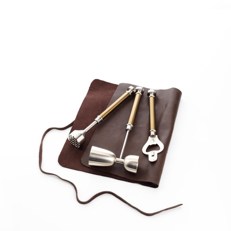 Set of bar tools including a mallet, ladle, and bottle opener on a brown leather mat with a white background.