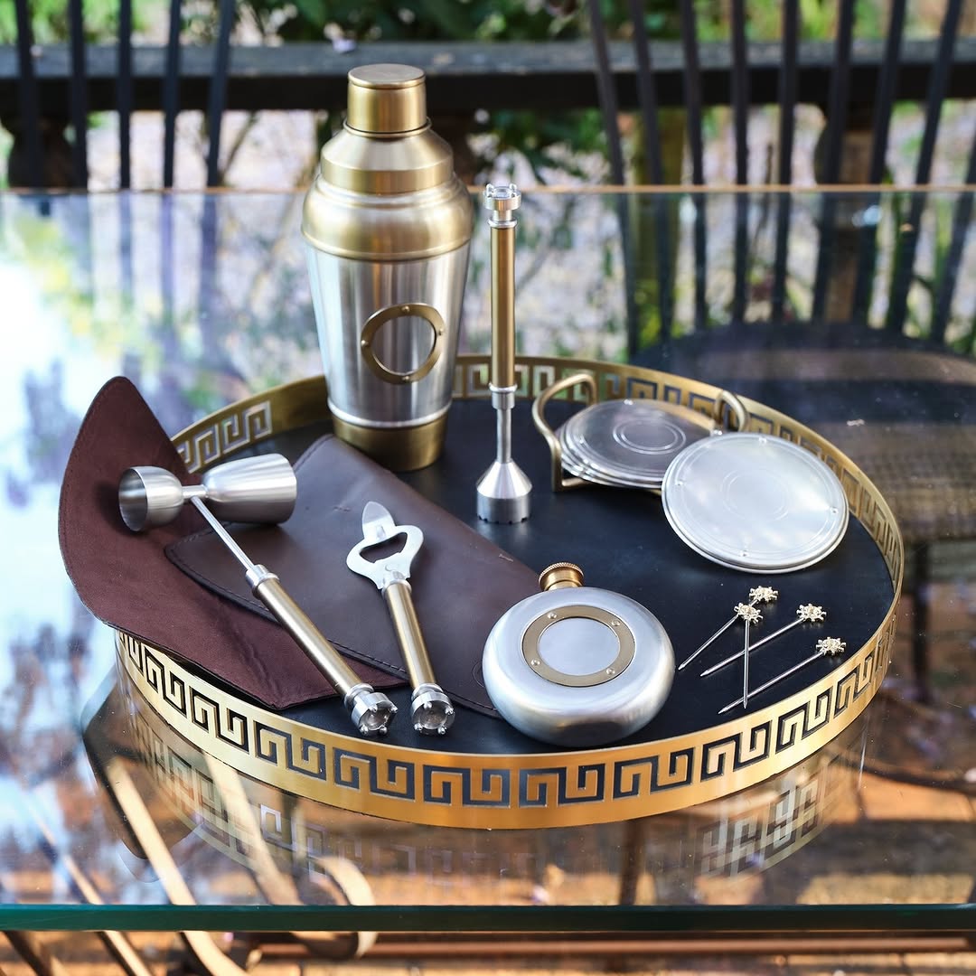 Bartender set with shaker, jigger, and other tools on a decorative tray outdoors.