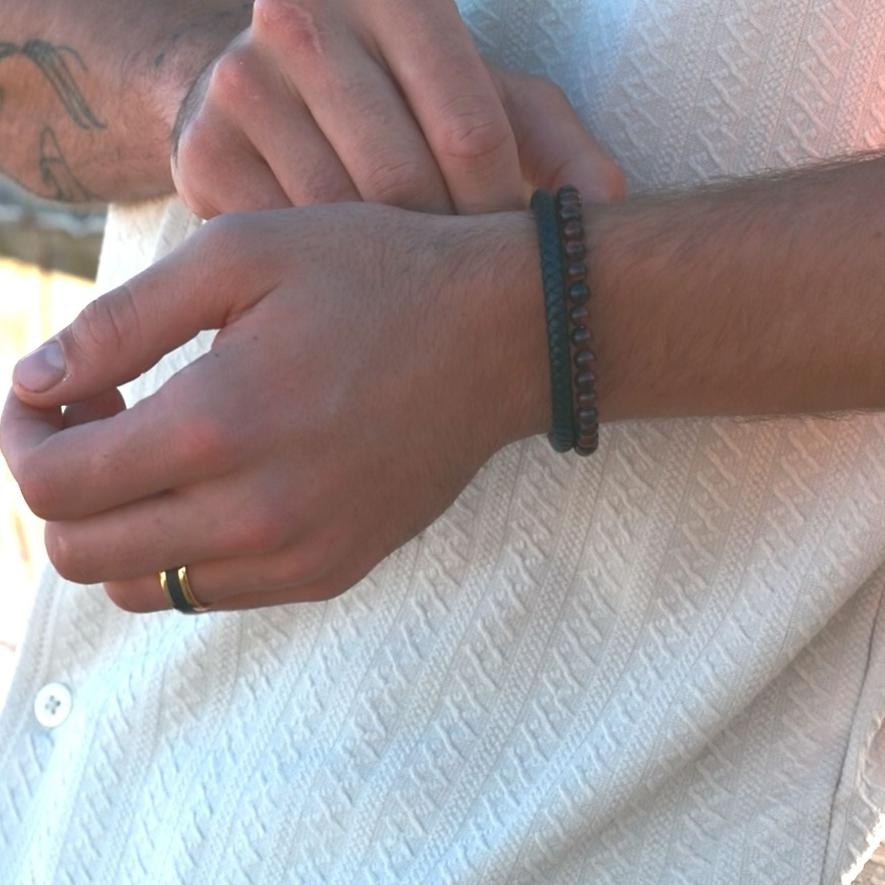 Close-up of a person's wrist with a bracelet and ring, wearing a white shirt.