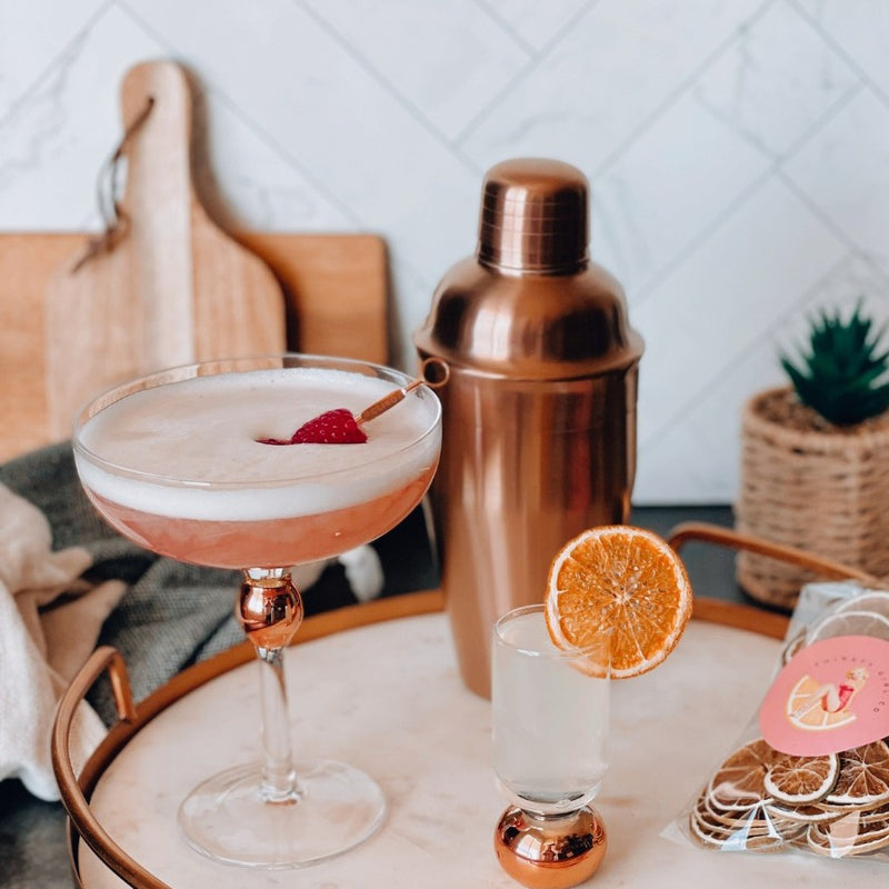 Cocktail setup with a glass, shaker, and garnishes on a tray.