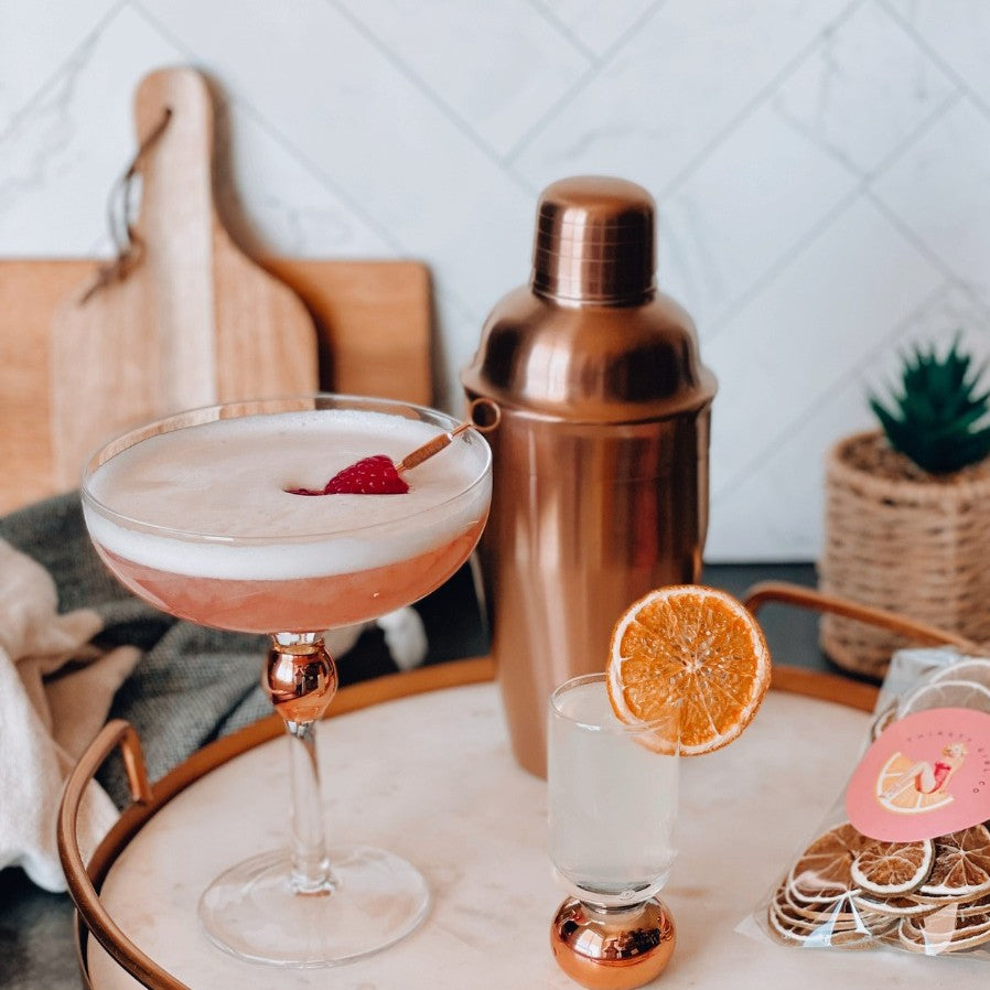 Cocktail setup with a glass, shaker, and garnishes on a tray.