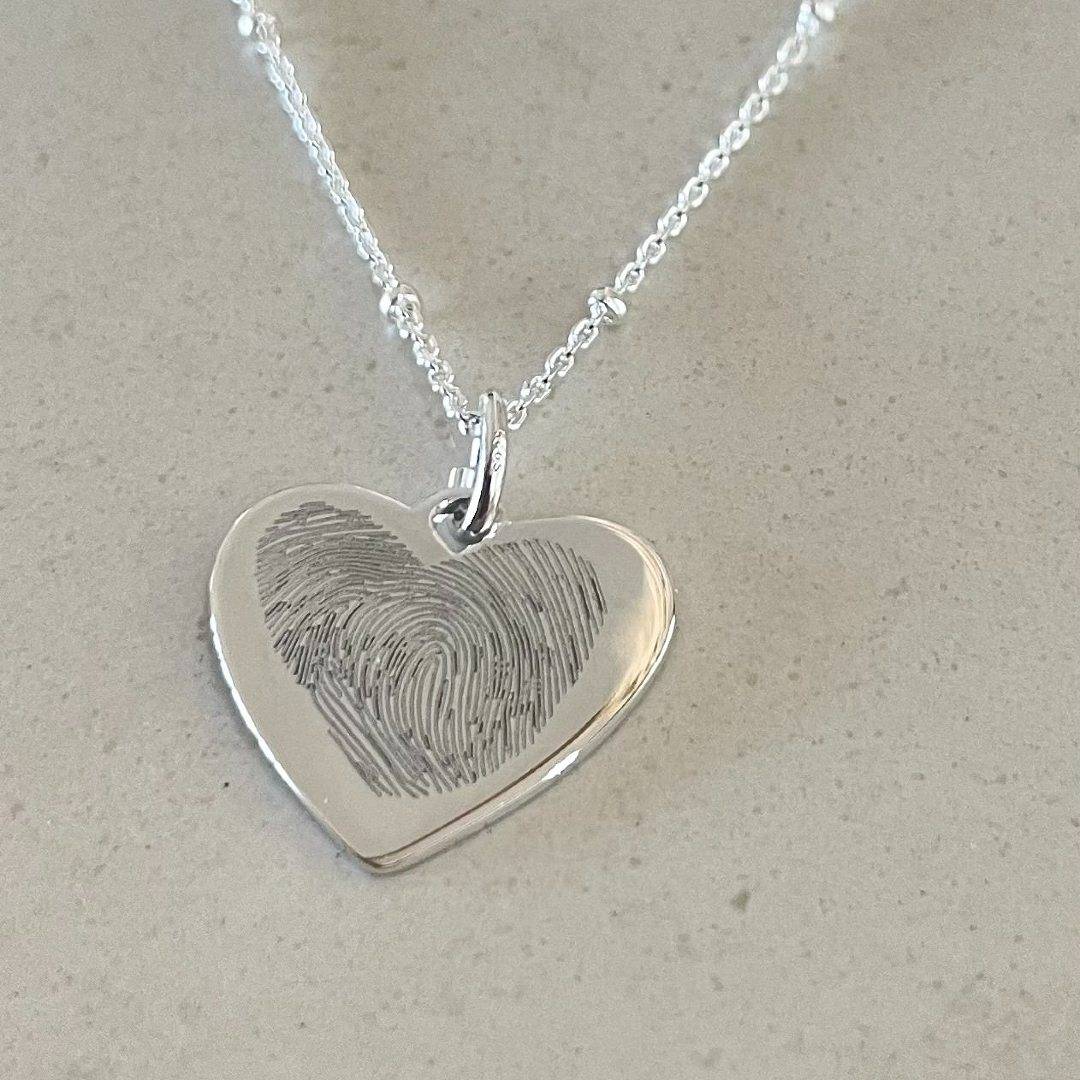 two fingerprint engraved in a heart shape on a silver necklace